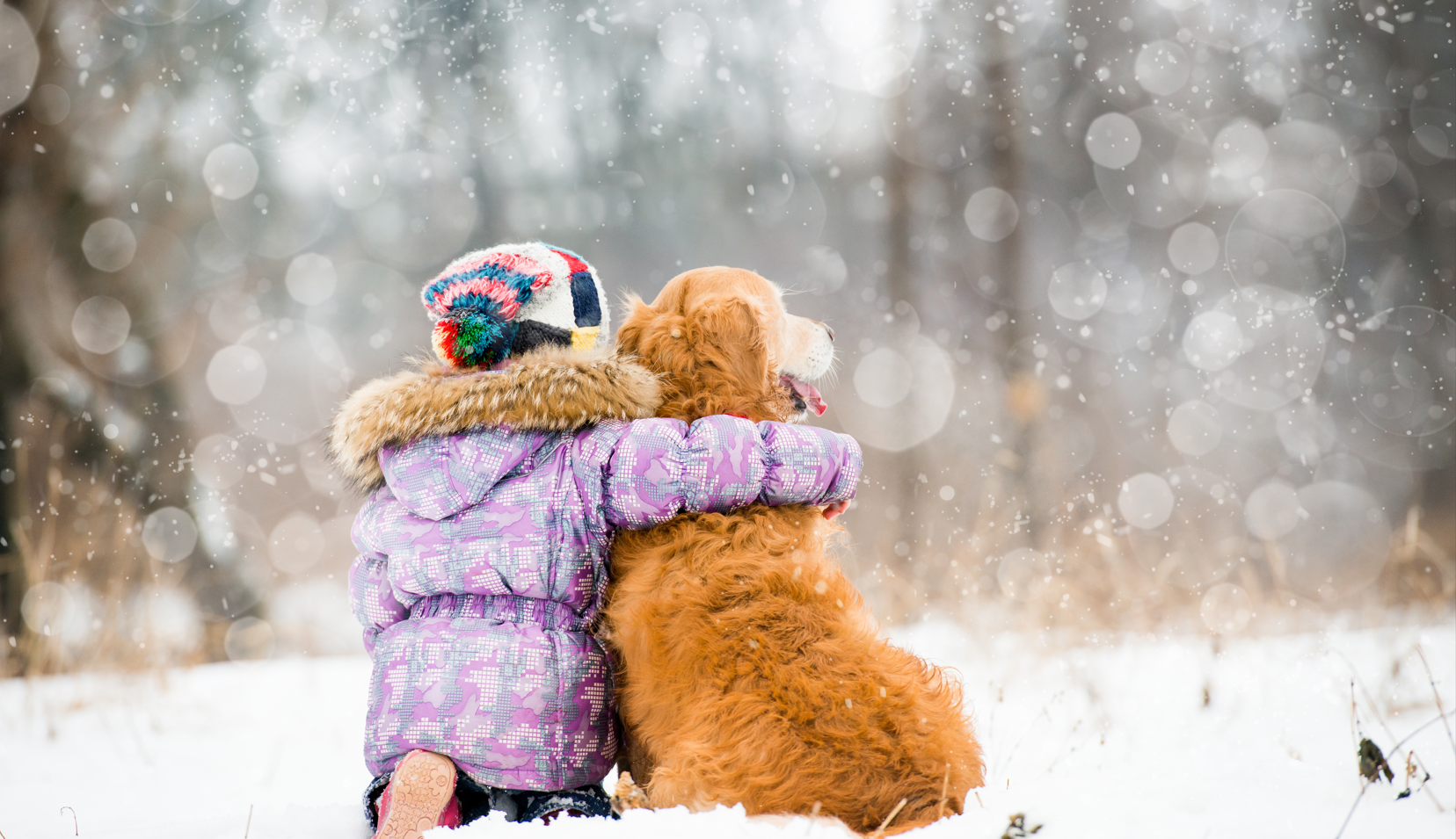 Child sitting in the snow, hugging a dog, enjoying a cozy and relaxed family moment with their pet during the Christmas break season